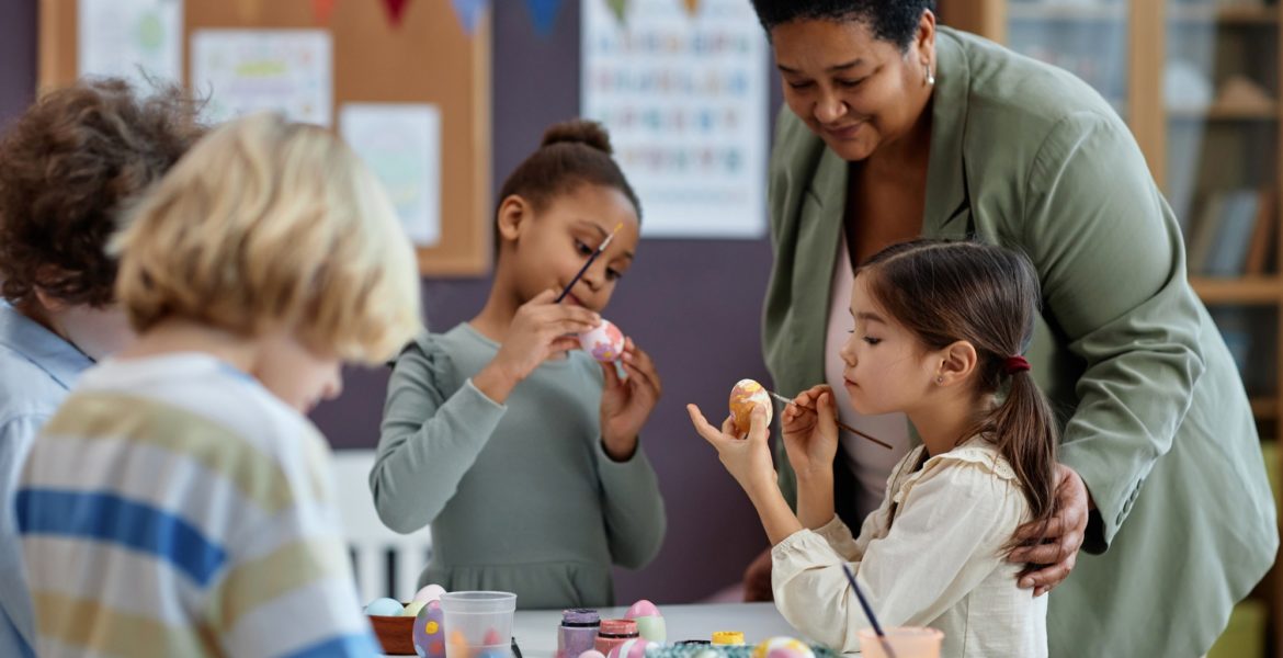 Diverse group of little kids painting Easter eggs enjoying arts and crafts class