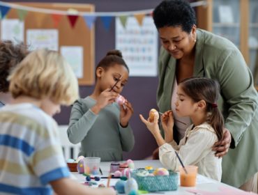 Diverse group of little kids painting Easter eggs enjoying arts and crafts class