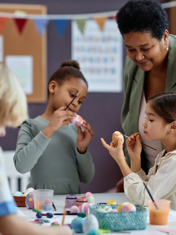 Diverse group of little kids painting Easter eggs enjoying arts and crafts class