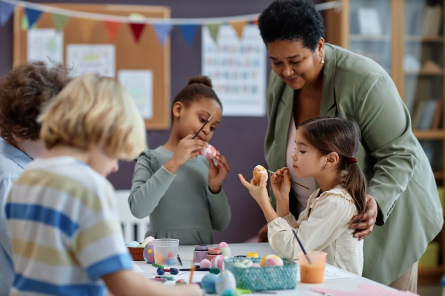 Diverse group of little kids painting Easter eggs enjoying arts and crafts class
